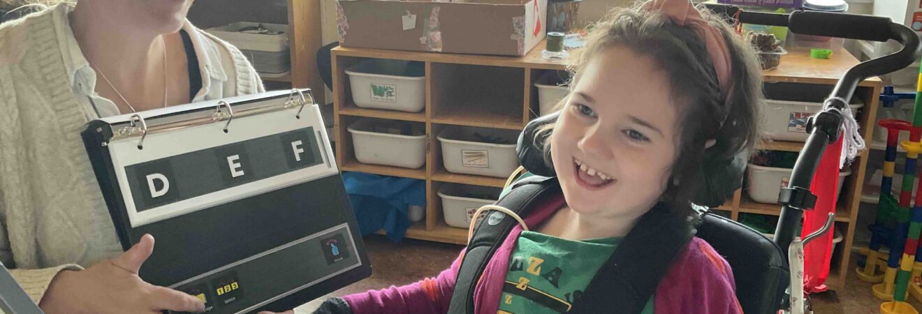 Girl smiling while looking at an alphabet flipchart.